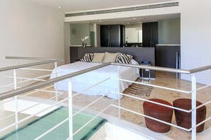 Ein modernes Schlafzimmer mit einem großen Bett, einem Balkon mit Glastrennwand und Blick auf den Pool.