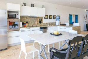 Eine moderne Küche mit weißen Schränken, einem Backofen, einer Mikrowelle und einem Geschirrspüler. Ein Esstisch mit Stühlen steht bereit, und auf der Arbeitsfläche befindet sich ein Wasserspender.