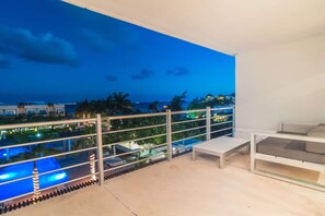 A balcony with a view of a swimming pool and a cityscape at dusk. - Beachside penthouse w/ pool & hot tub (Playa del Carmen)