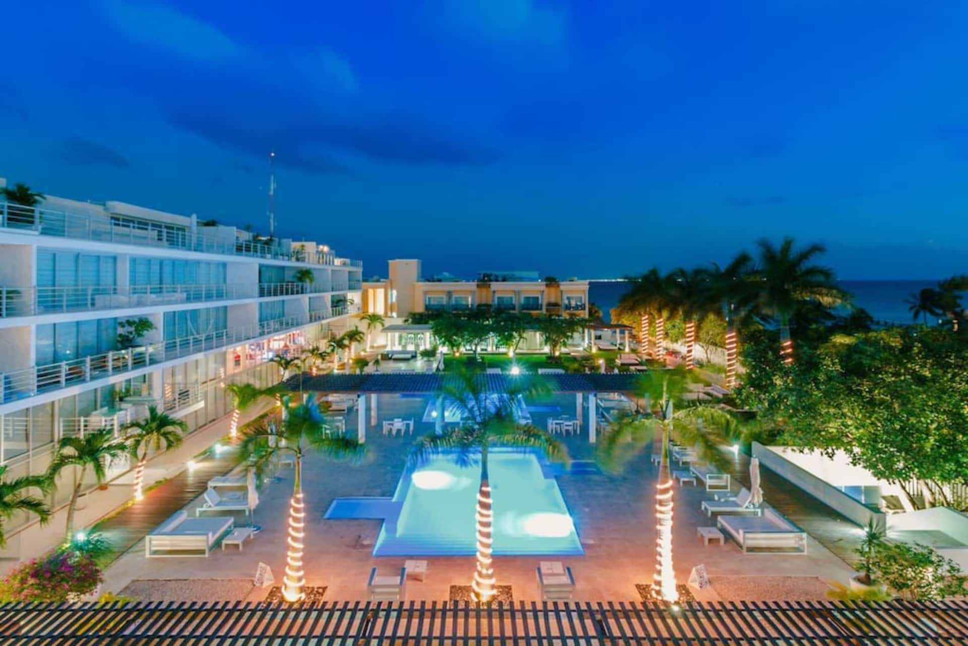 A hotel pool area with multiple levels of balconies, a central pool, and lounge chairs.