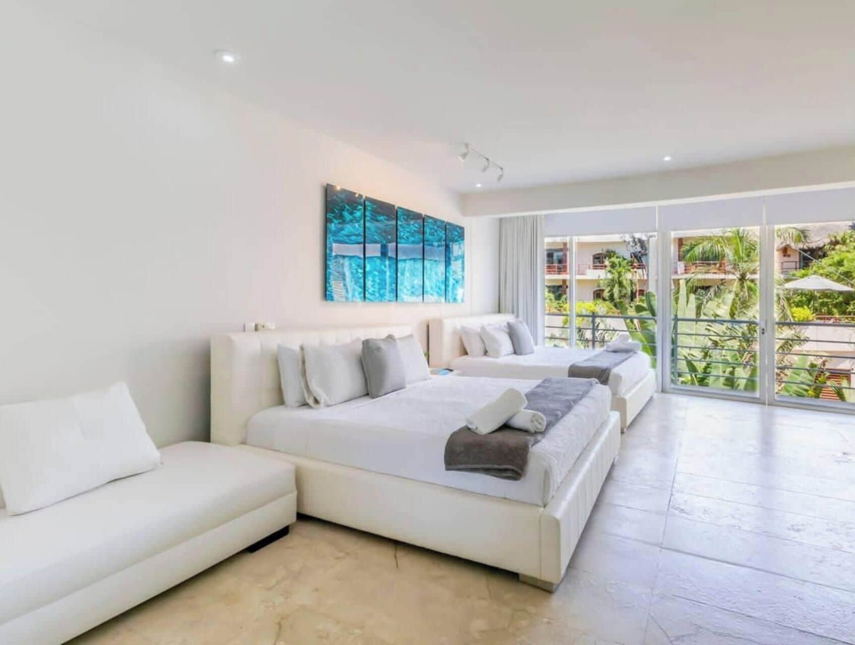 A modern hotel room with a large bed, a sofa, and a balcony with a view of greenery.