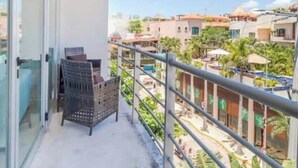A balcony with a chair and a table, overlooking a residential area with buildings and greenery. - Beachside escape w/ pool & balcony (Playa del Carmen)