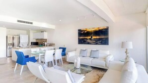 A modern living room with a sofa, chairs, a glass coffee table, and a dining area with a kitchen in the background. - Beachside escape w/ pool & balcony (Playa del Carmen)