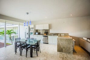 Een moderne keuken met witte kasten, een granieten aanrechtblad en een eethoek met een glazen tafel en zwarte stoelen.
