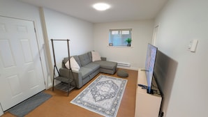 A living room with a sectional sofa, a standing fan, a TV, and a window with blinds. - Willoughby Nest in Langley Township - Perfect Family Getaway (Langley)