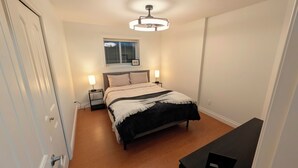 A bedroom with a bed, bedside lamps, a ceiling fan, a window with blinds, and a door. - Willoughby Nest in Langley Township - Perfect Family Getaway (Langley)