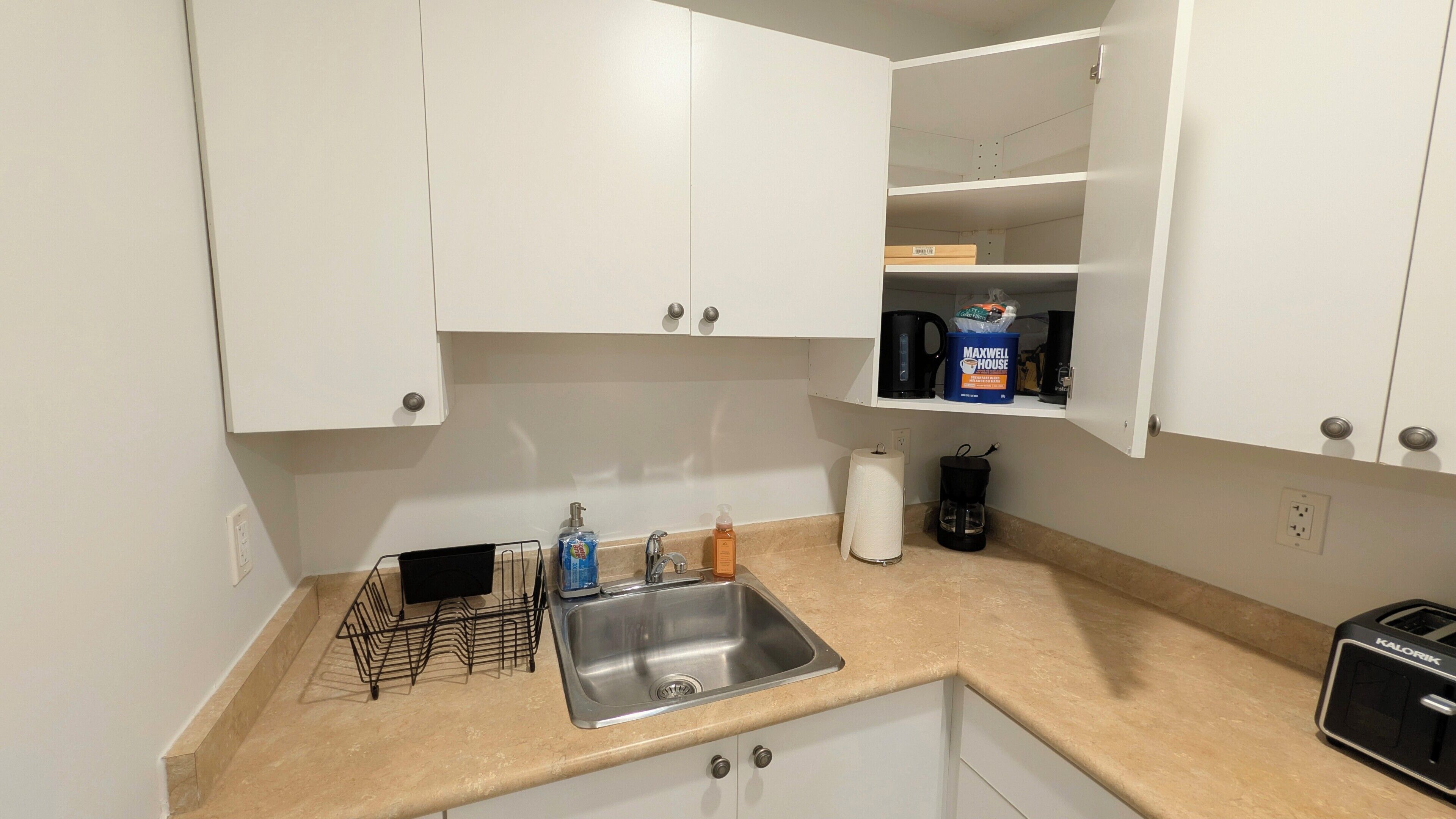 A kitchen with white cabinets, a stainless steel sink, a coffee maker, and a toaster.