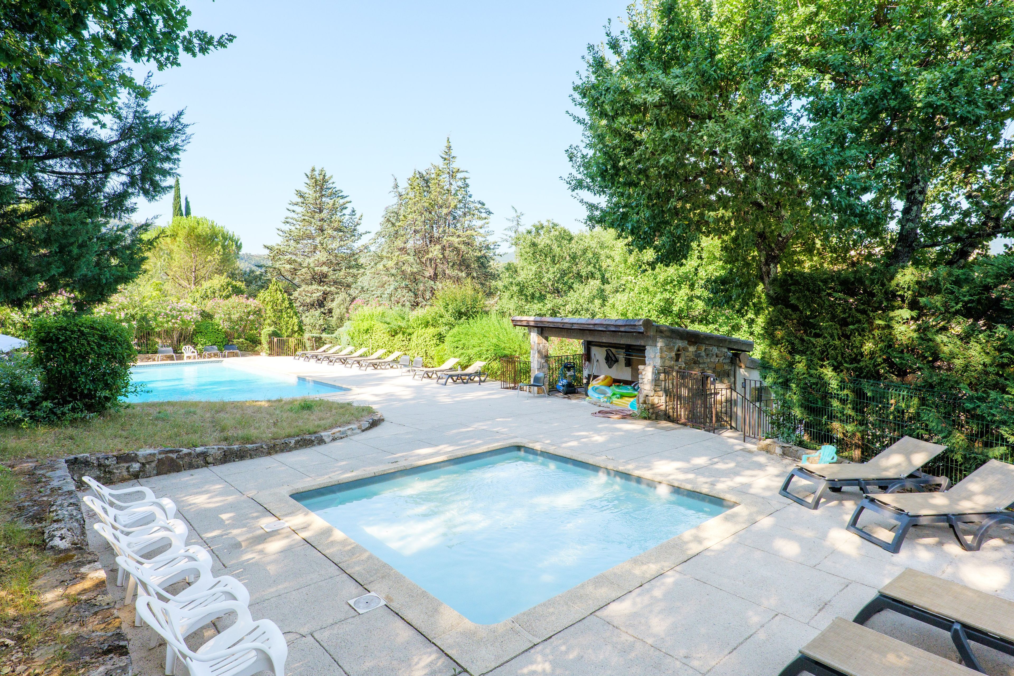 Ein Garten mit Swimmingpool, Liegestühlen und Grillplatz.