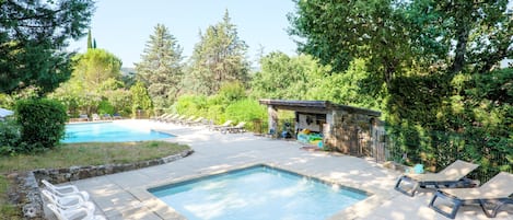 Ein Garten mit Swimmingpool, Liegestühlen und Grillplatz.