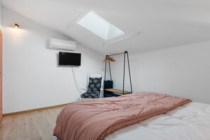 Una camera da letto con un lucernario, un letto con coperta fantasia, una sedia a dondolo e un televisore a parete.