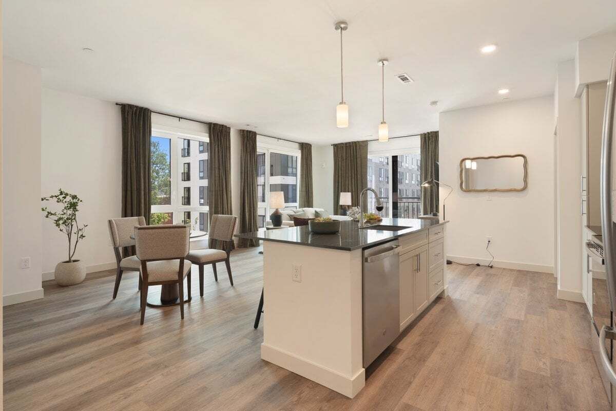 Una cocina moderna con una isla central, comedor con sillas y ventanas amplias.
