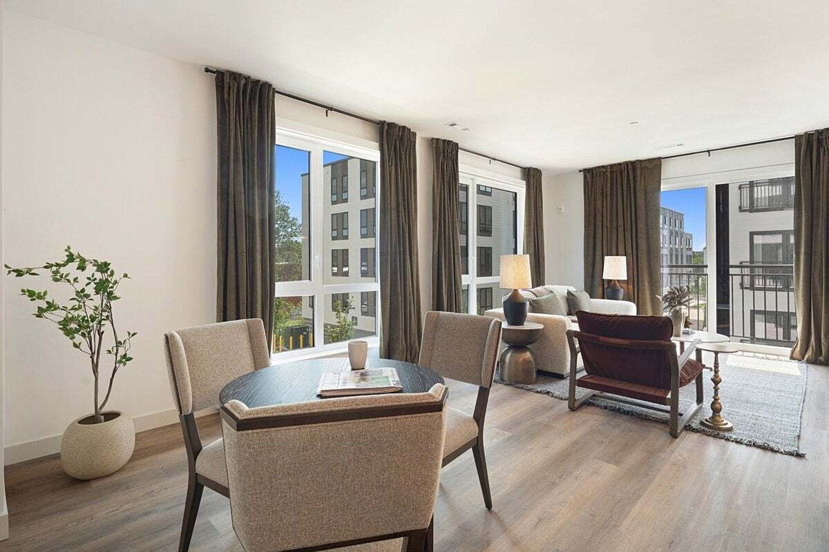 Habitación de hotel moderna con zona de comedor, sofá, lámpara y vistas a la ciudad.