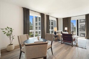 Habitación de hotel moderna con zona de comedor, sofá, lámpara y vistas a la ciudad.