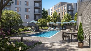 Une piscine entourée d’immeubles d’habitation et de verdure, avec des chaises longues et des parasols.
