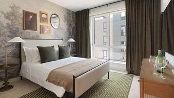 Habitación de hotel con cama, lámparas de noche, cómoda, ventana con cortinas y vistas al exterior.