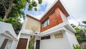 Una casa moderna de dos pisos con fachada blanca, un muro decorativo de madera y un pequeño jardín.