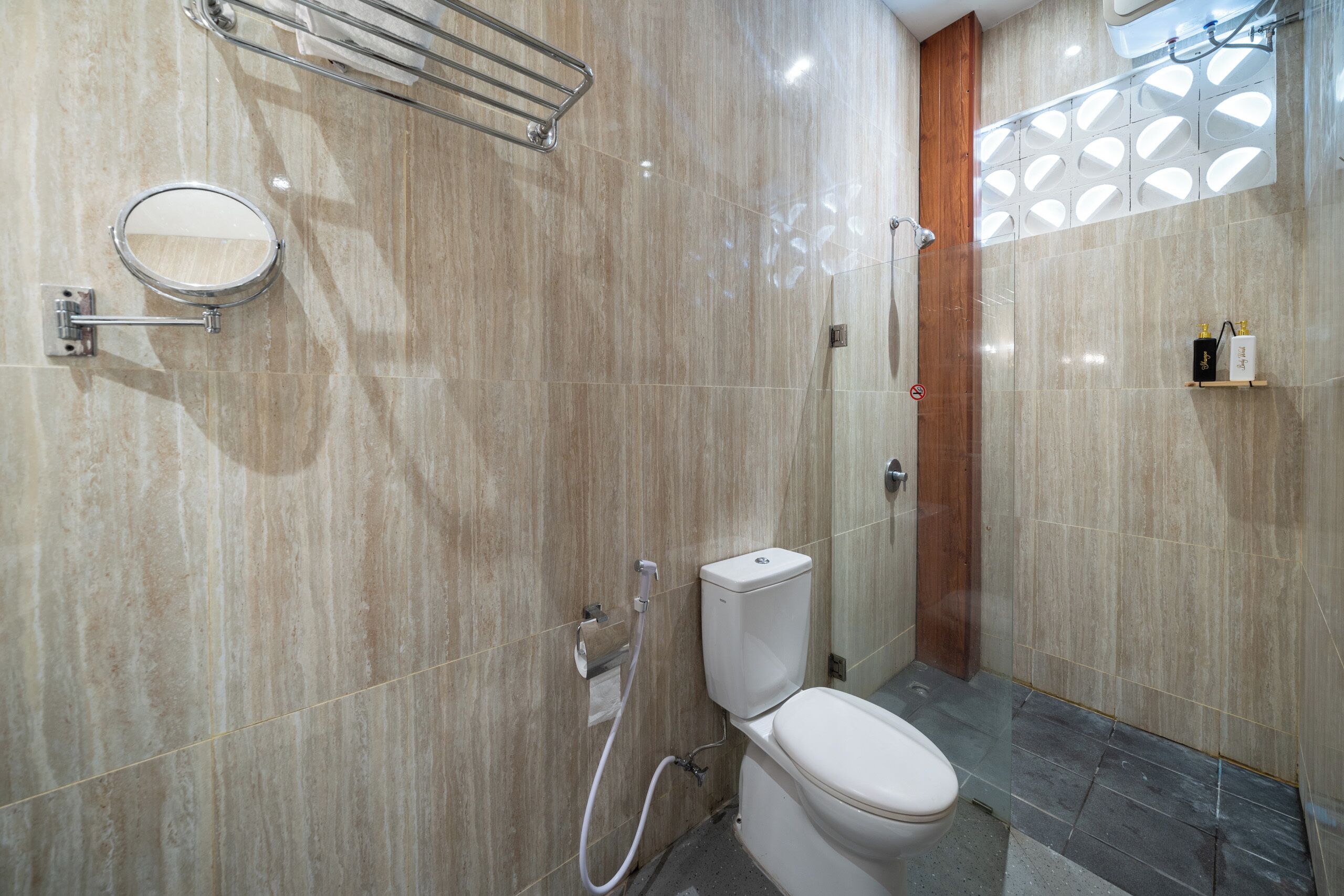 A modern bathroom with a toilet, a shower, a mirror, and a shelf with toiletries.