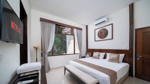 Habitación de hotel con cama, un banco, un televisor mostrando 'NETFLIX' y una ventana con cortinas.