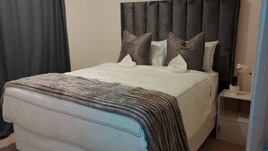 A neatly made bed with a grey and white duvet, a dark headboard, and a bedside table with a vase of flowers. - Room-luxurious 2-bedroom Apartment in Ja (Johannesburg)
