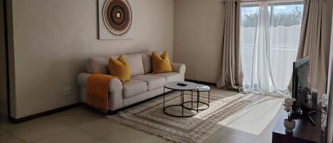 A living room with a sofa, a coffee table, a rug, a TV, and a window with curtains.