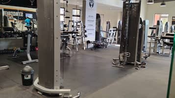 Uma academia com equipamentos de ginástica, um banner com palavras motivacionais e uma lixeira.