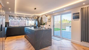 Een moderne keuken met een groot eiland, inbouwapparatuur en een schuifdeur naar een terras.