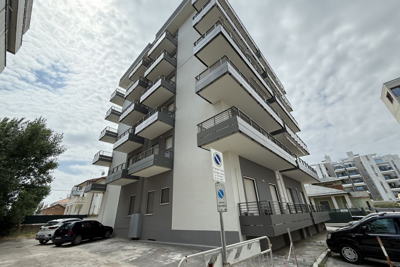 A multi-story residential building with balconies, a parking area, and a sign indicating a no parking zone.