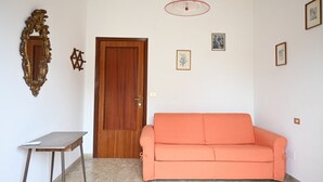 A room with a wooden door, a small table, an orange sofa, and a pendant light. - SE293 - Senigallia, two-room apartment just steps from the sea and the center of Senigallia. (Senigallia)