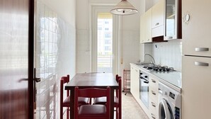 A narrow kitchen with a dining table and chairs, a washing machine, and cabinets. - SE293 - Senigallia, two-room apartment just steps from the sea and the center of Senigallia. (Senigallia)