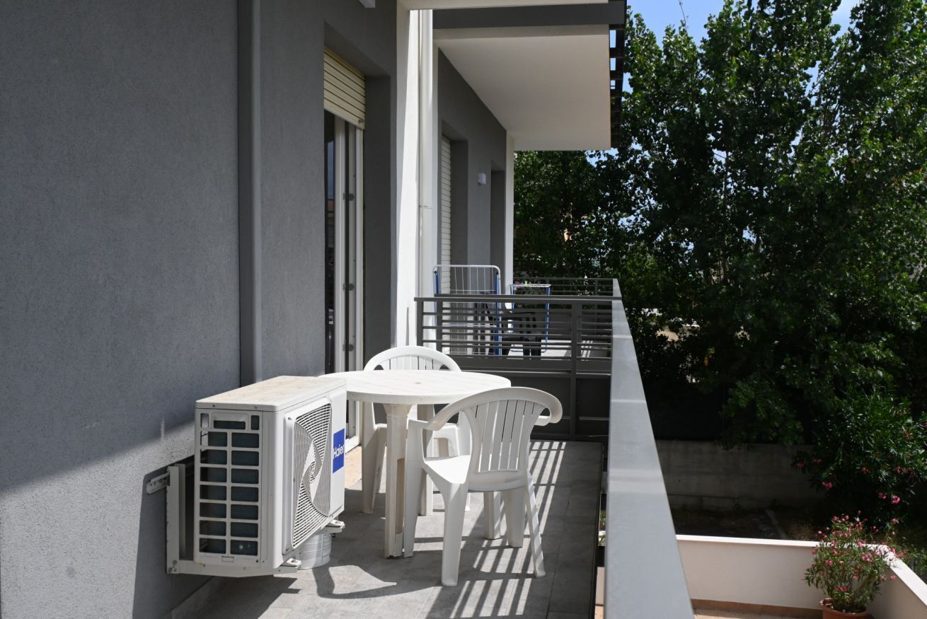 A balcony with a table and chairs, an air conditioning unit, and a railing.