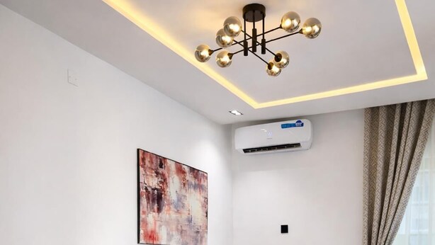 Una camera d'albergo moderna con un divano, un tavolino, una lampada, un letto con copriletto blu, un tappeto decorato e un condizionatore d'aria.