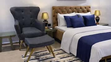 A bedroom with a tufted headboard bed, a grey armchair, a patterned rug, and a modern abstract painting.