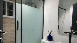Un bagno moderno con cabina doccia in vetro, un water bianco, un mobile lavabo nero con lavandino bianco e uno specchio sopra il lavandino.