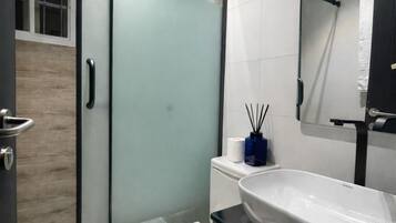 A modern bathroom with a glass shower enclosure, a white toilet, a black vanity with a white sink, and a mirror above the sink.