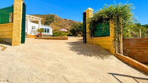 A gated entrance with a white building in the background, a clear sky, and a hilly landscape. - Cortijo las Flores con Piscina Privada (Torrox)