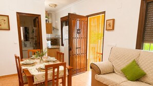 A dining area with a table set for four, a sofa with a green pillow, and a sliding door leading to a kitchen. - Cortijo las Flores con Piscina Privada (Torrox)