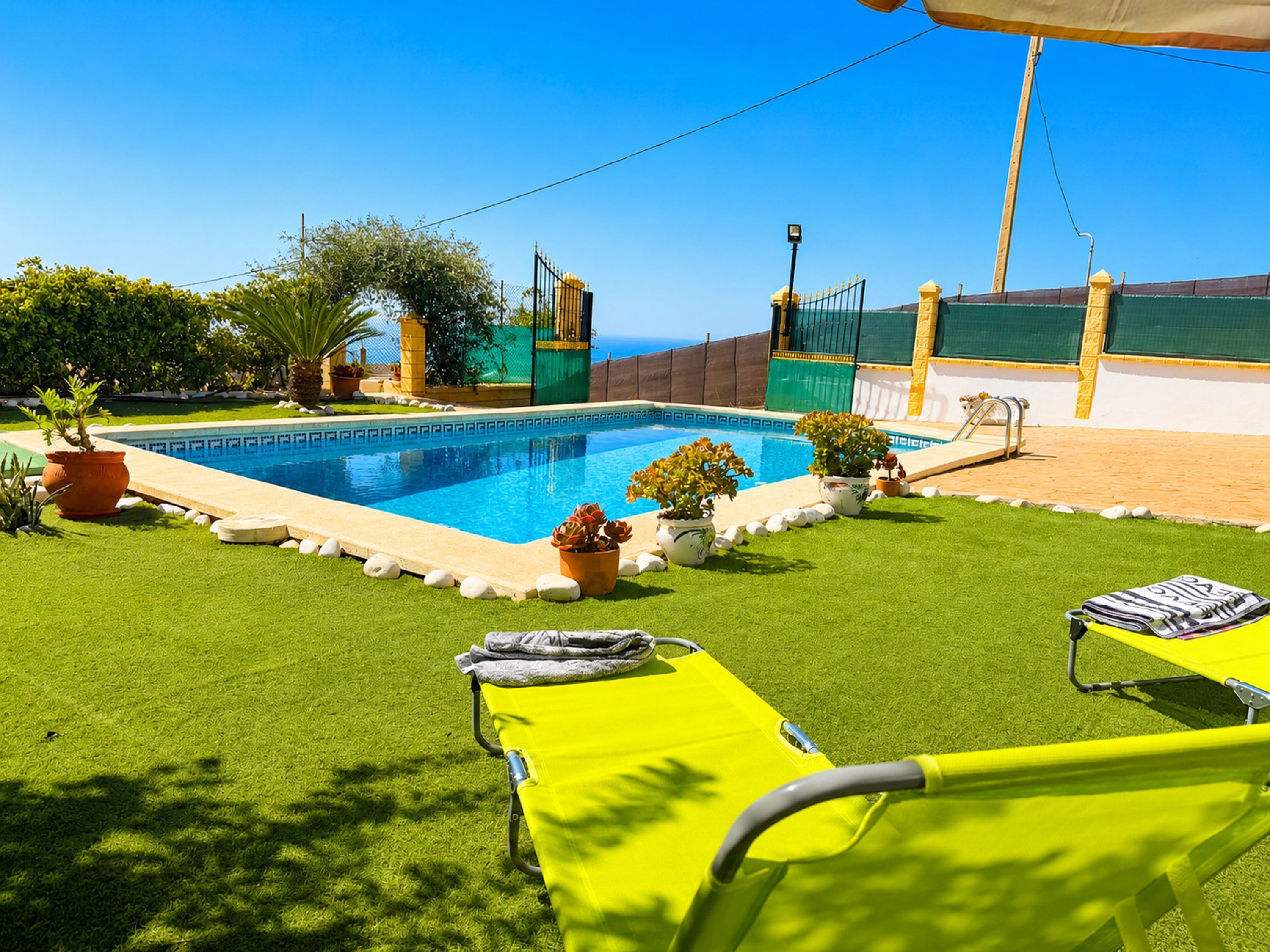A swimming pool with a clear view of the sea, surrounded by a well-maintained lawn and potted plants.