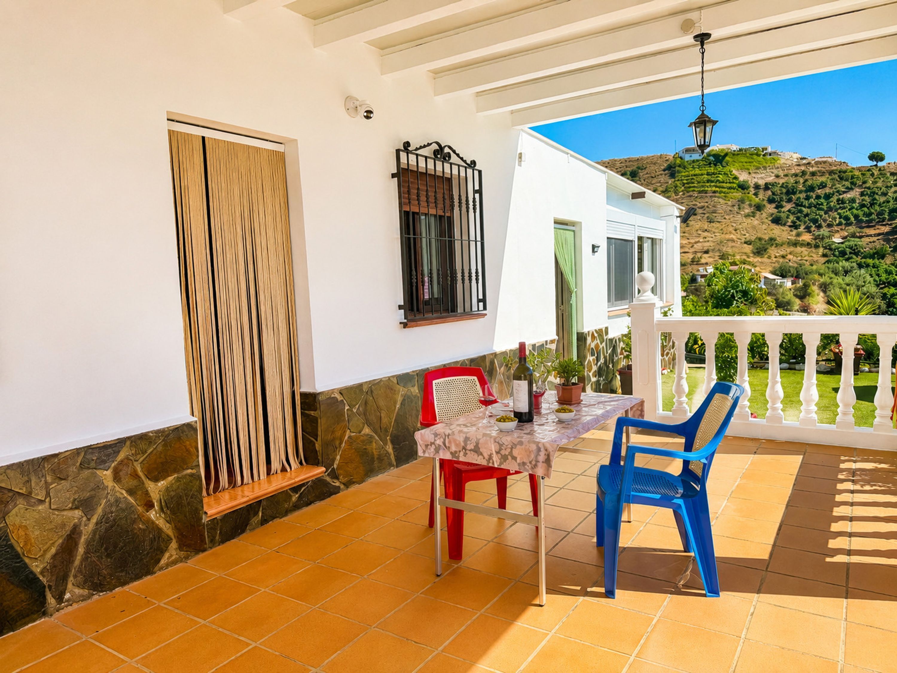 A patio with a table and chairs, a window with a curtain, and a view of a hillside.