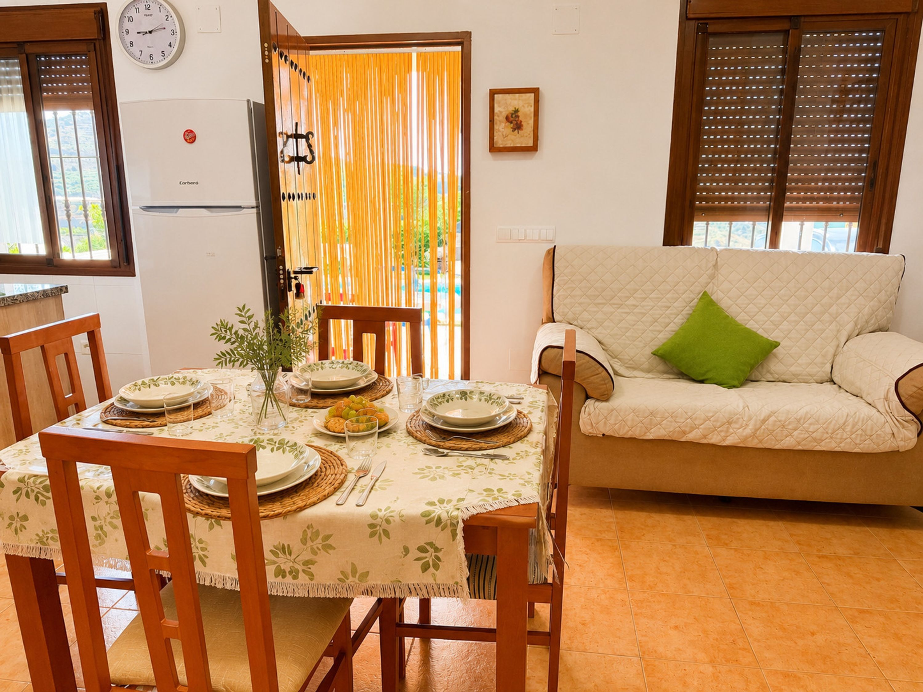 A dining area with a table set for four, a sofa, and a kitchen visible in the background.