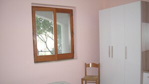 Un dormitorio con una cama, una silla de madera, un armario y una ventana.