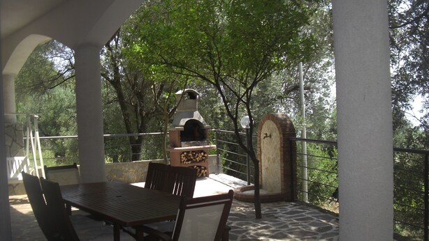 Un patio al aire libre con una mesa y sillas de piedra, un horno para pizza y un muro de piedra.