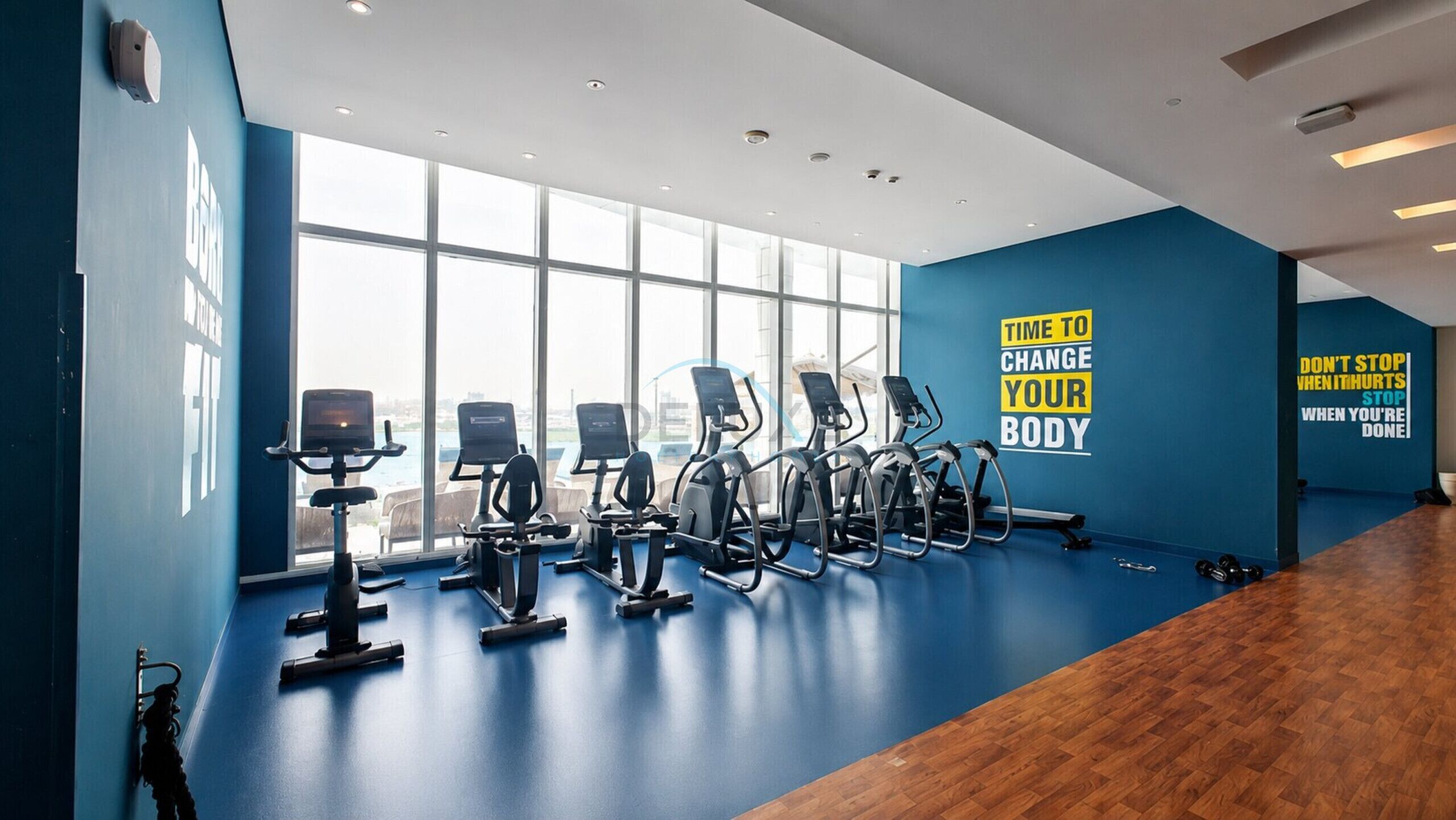 A gym with exercise equipment, large windows, and motivational wall decals.
