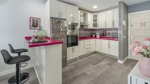 A modern kitchen with white cabinets, a pink countertop, a refrigerator with magnets, a microwave, and a sink. - Charming 2-bedroom Apartment in Puerto de Santiago (Santiago del Teide)