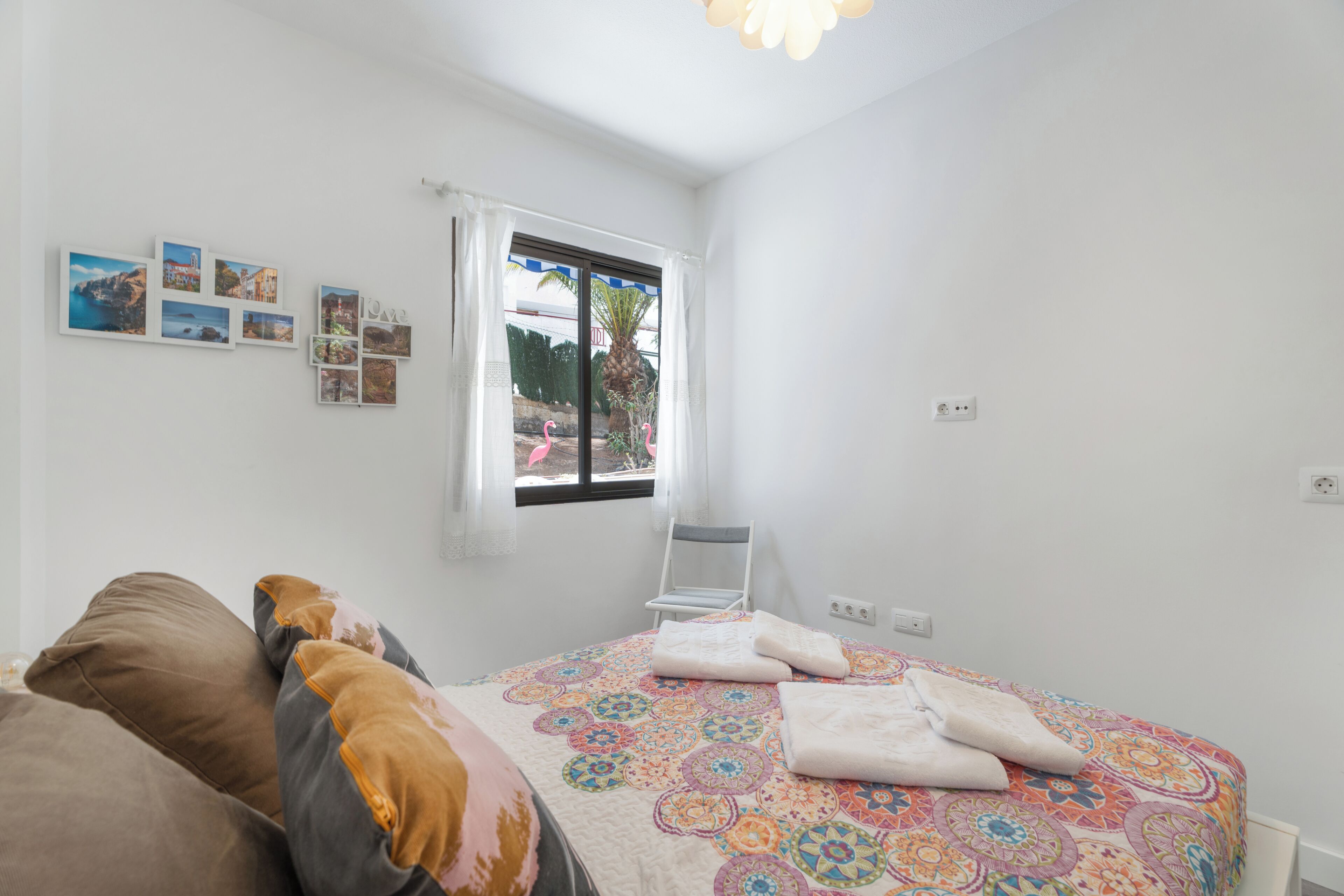 Un dormitorio con cama, almohadas, una silla, un ventanal y decoración en la pared.