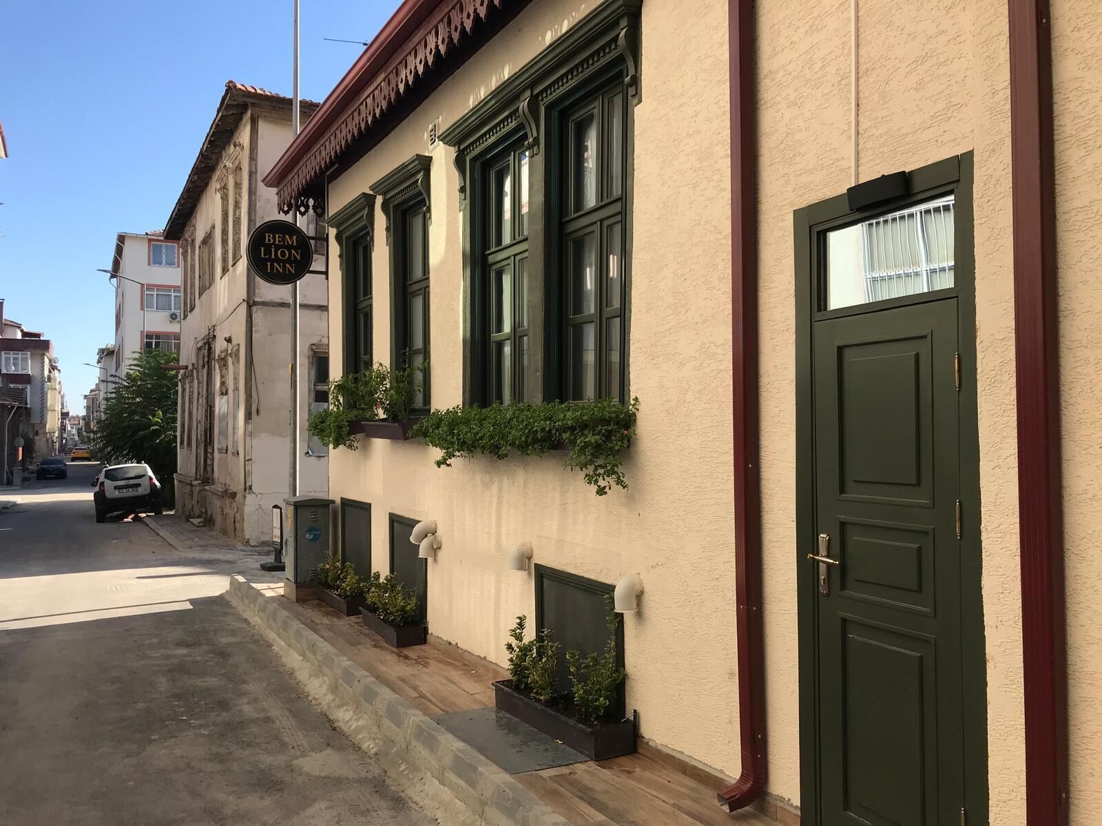 Um edifício com porta verde, uma placa acima da porta e uma janela com uma planta.