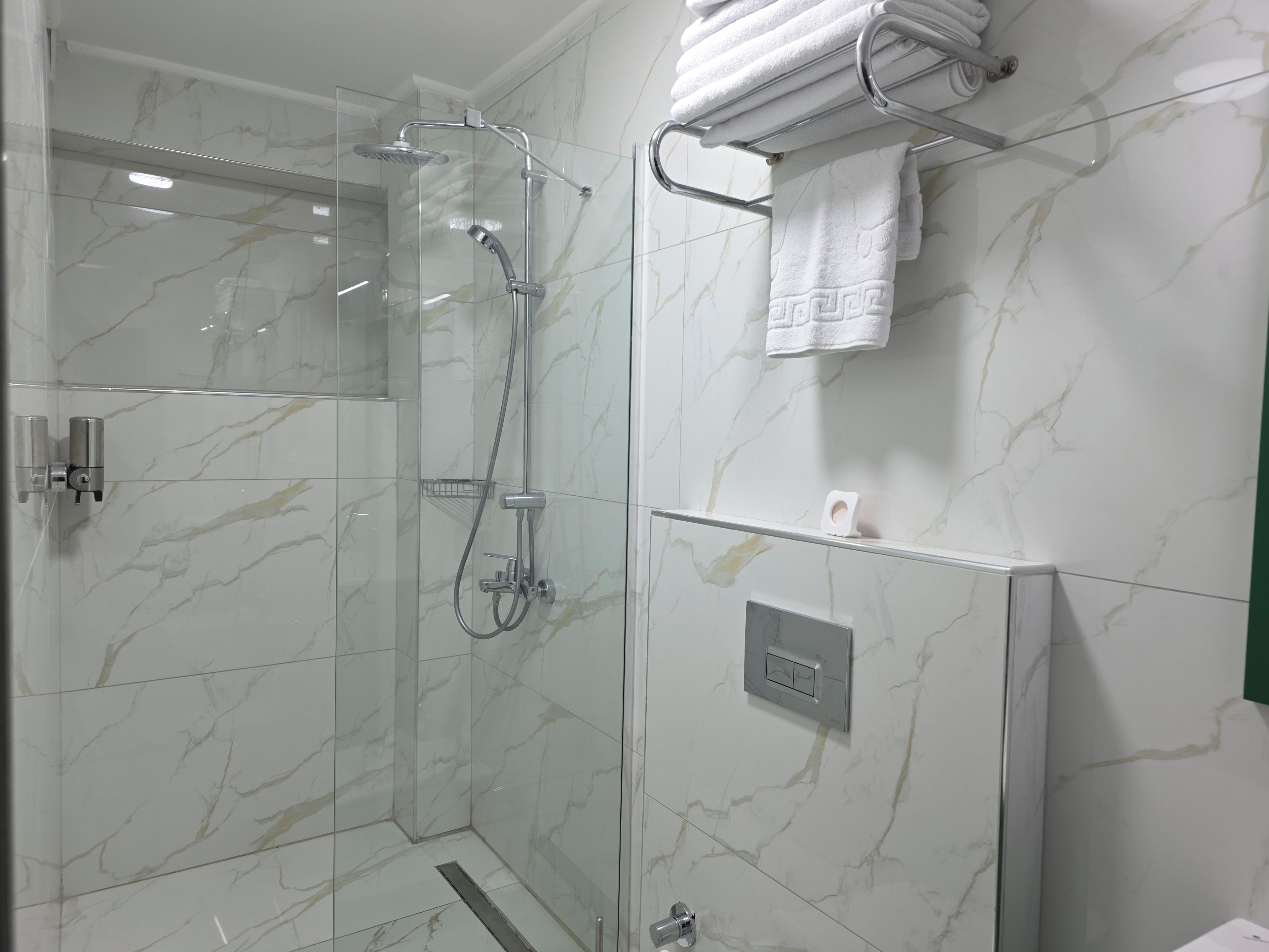 Un baño moderno con ducha de vidrio, un perchero para toallas y un dispensador de papel higiénico.