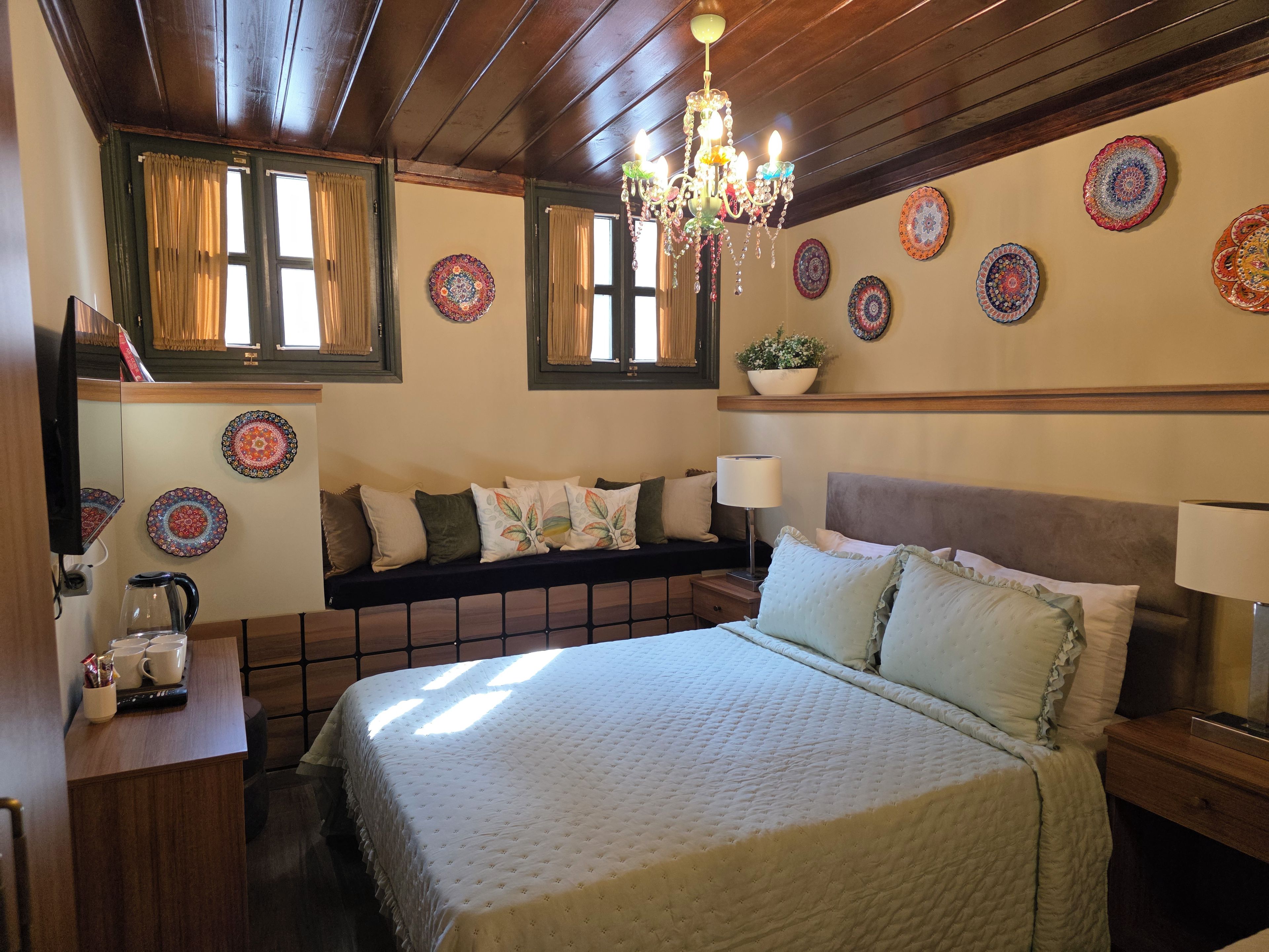 Una camera da letto con un letto, comodini, un lampadario, un divano e piatti decorativi alle pareti.