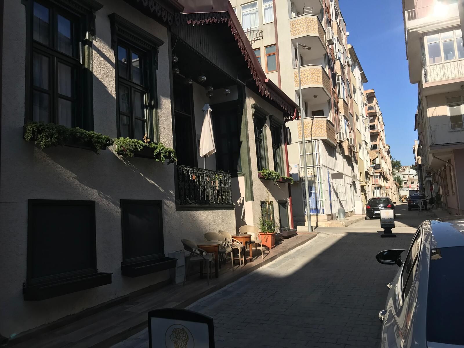 A narrow street lined with multi-story buildings, some with balconies and outdoor seating.