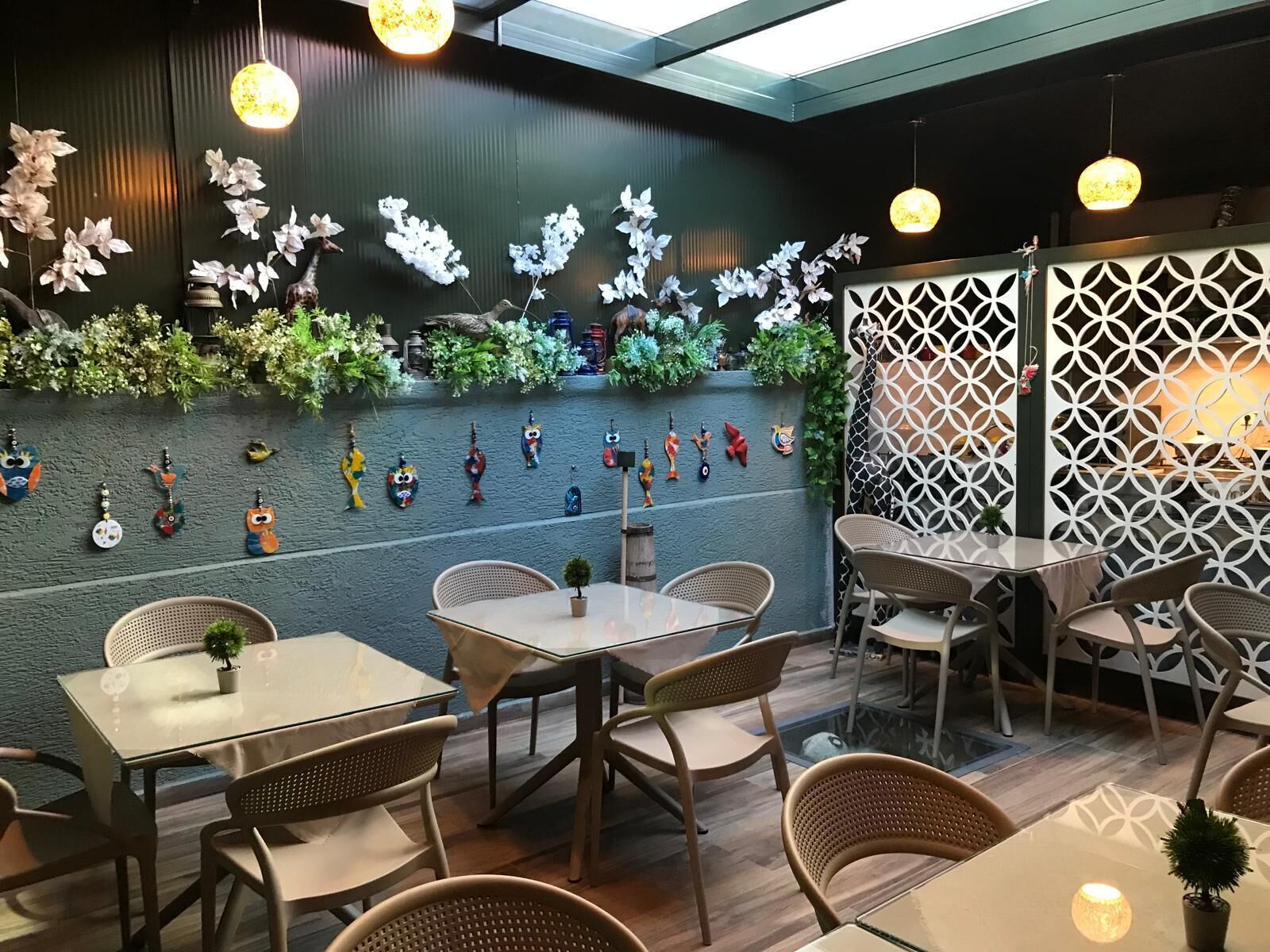 Espaço de refeições interno com mesas, cadeiras, arte decorativa nas paredes e luminárias pendentes.