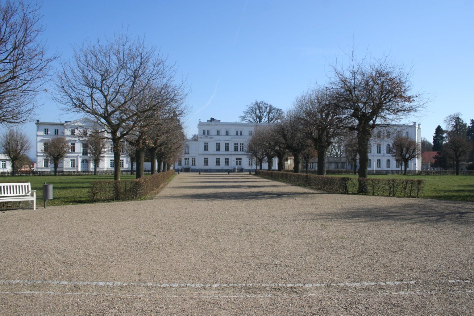A gravel pathway leading to a large white building with multiple windows and a symmetrical facade.